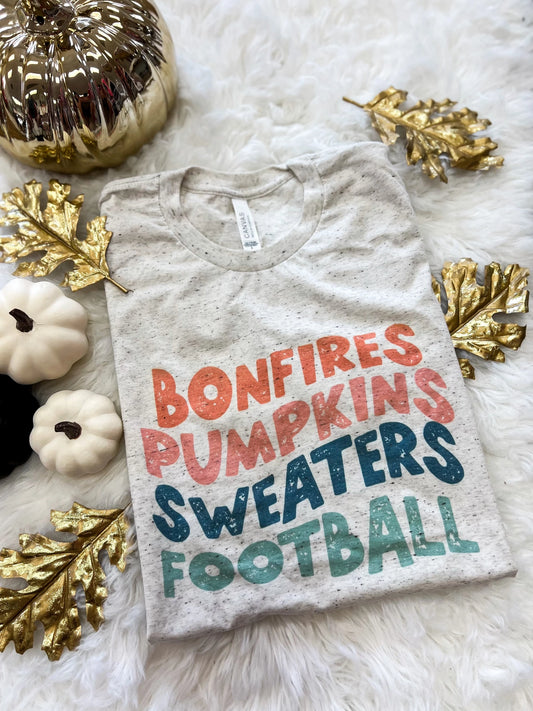 fall tee in neutral oatmeal with the phrase bonfires, pumpkins, sweaters, and football